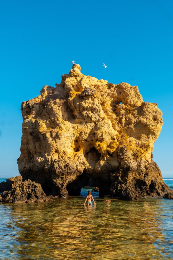 A tourist in the water next to the rocks at Praia dos Arrifes, Algarve beach, Albufeira. Portugal
